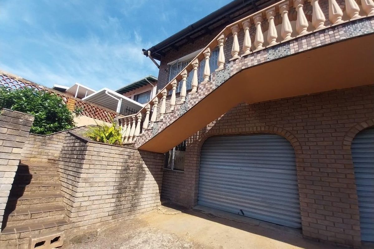 Rear exterior view showing a brick facade, external staircase with balustrade, and double roller shutter garage doors.