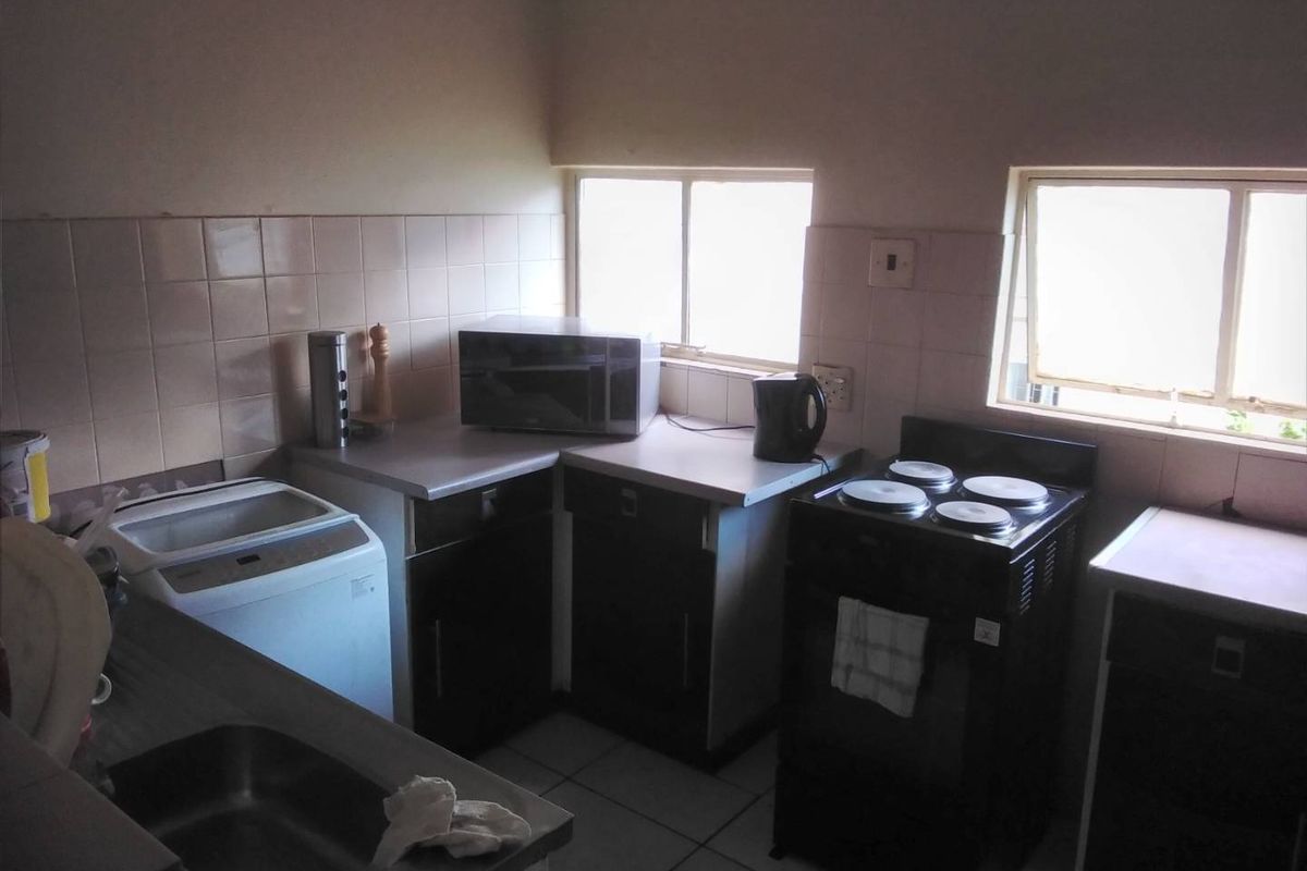 A functional kitchen featuring built-in cabinetry, laminate countertops, a stainless steel sink, and a freestanding stove with tiled backsplash and flooring.