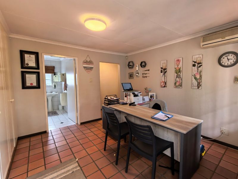 A functional office space featuring durable tiled flooring, an integrated air conditioning unit, and direct access to an adjacent bathroom.
