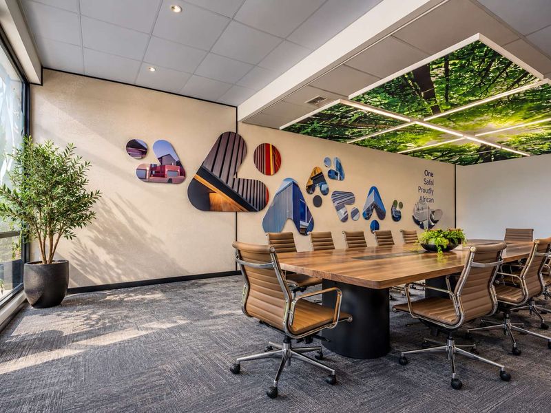 A modern, well-maintained office boardroom featuring a large wooden conference table, carpeted flooring, and a unique integrated ceiling design with natural imagery.