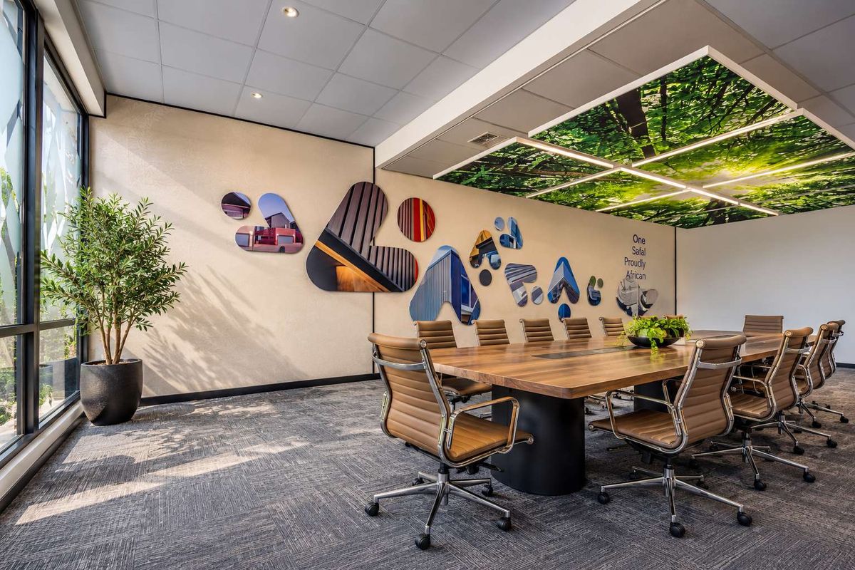 A modern, well-maintained office boardroom featuring a large wooden conference table, carpeted flooring, and a unique integrated ceiling design with natural imagery.