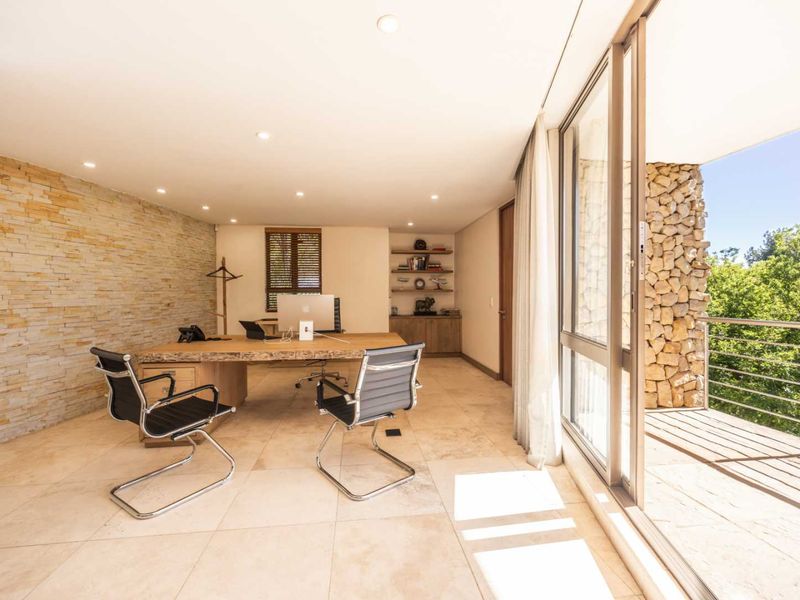 Modern office space featuring a stone accent wall, built-in shelving, and large sliding glass doors opening onto a private balcony with natural light.