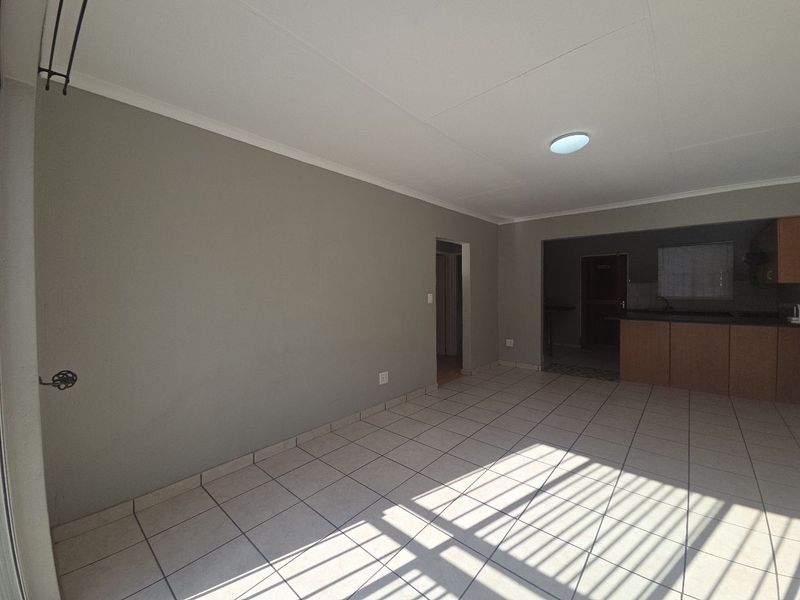 An open-plan living area featuring neutral tiled flooring, a simple ceiling light, and a view into the adjacent kitchen space.