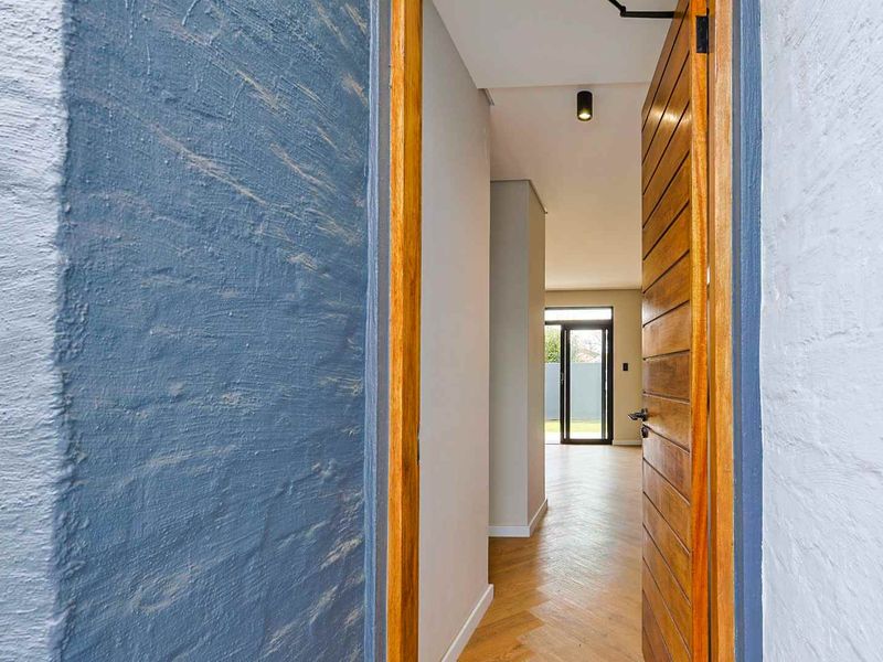 A bright entrance featuring a natural timber door, textured blue brick wall, and elegant herringbone timber flooring leading into the main living area.