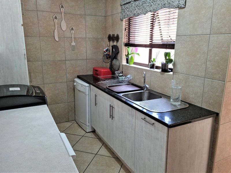 A functional scullery area featuring built-in cabinetry, granite countertops, a stainless steel sink, and tiled finishes throughout.