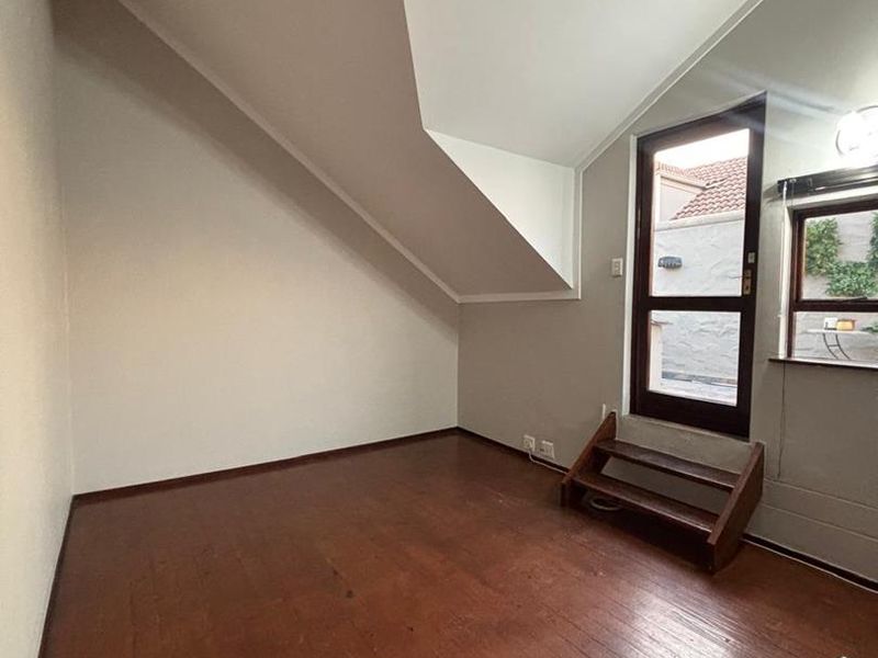 An empty bedroom featuring timber flooring, a unique sloped ceiling, and direct access to an outdoor area via a glass panel door.
