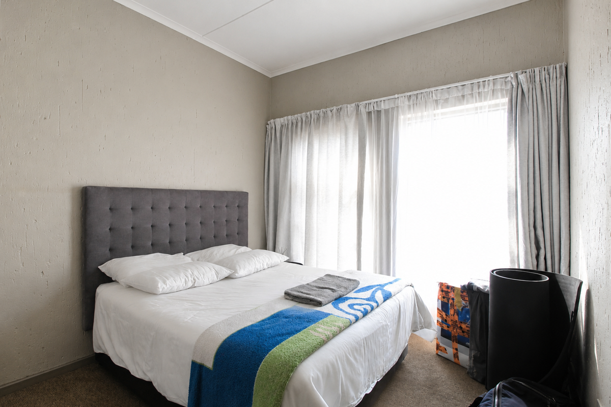 A bedroom featuring neutral textured walls, carpeted flooring, and a large window with floor-to-ceiling curtains allowing for natural light.