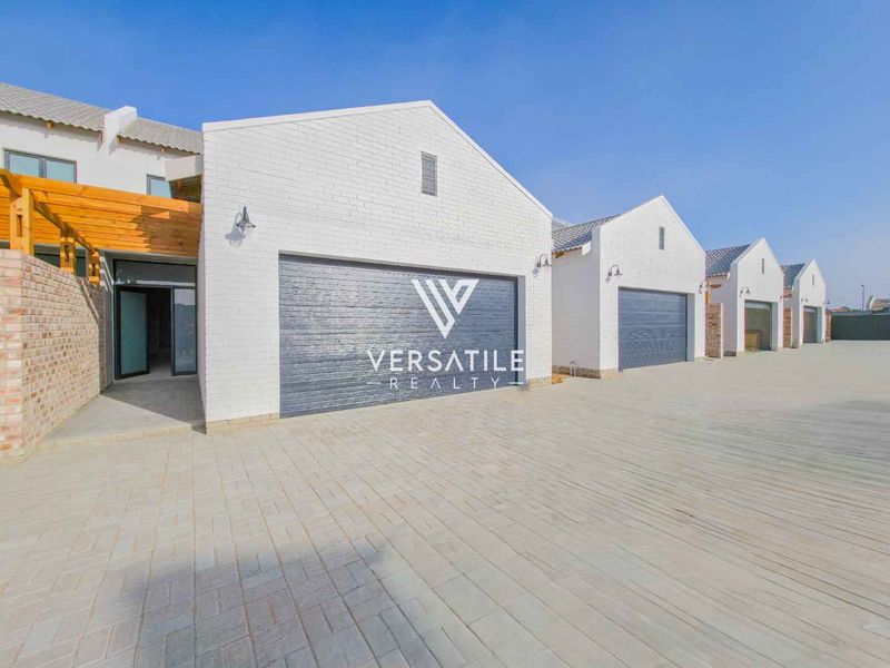 Modern townhouse exterior featuring white brick facade, paved driveway, and multiple sectional garage doors with timber pergola detail.