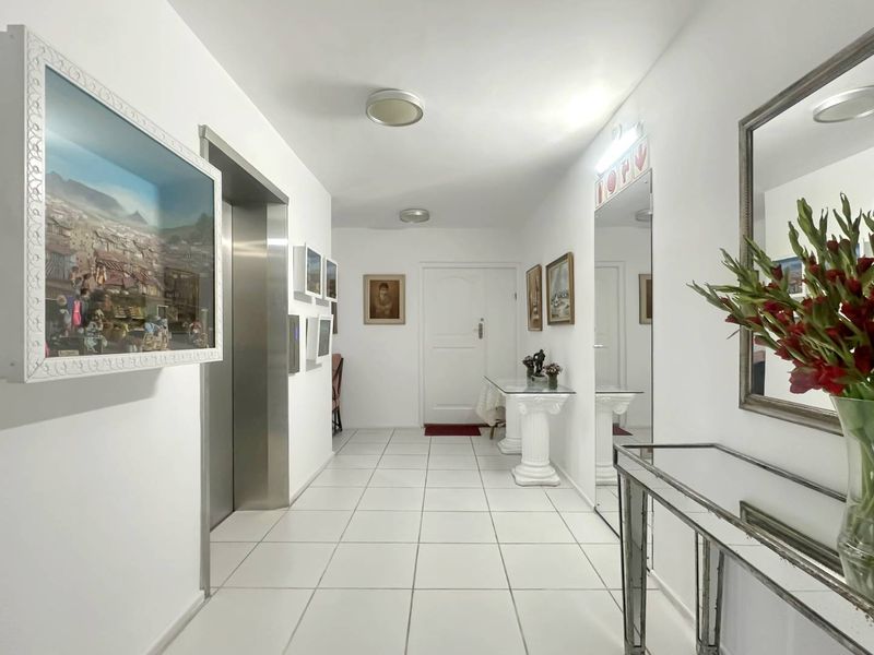 A bright and well-maintained apartment hallway featuring tiled flooring, a private elevator access point, and a large wall-mounted mirror.
