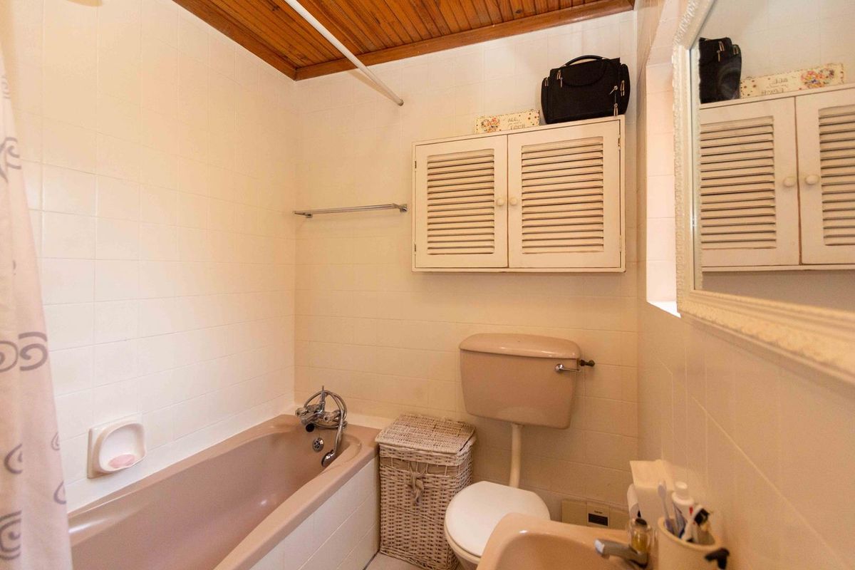 A dated bathroom featuring a colored bathtub, toilet, and washbasin with timber ceiling paneling and wall-mounted storage cabinetry.