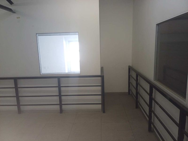 An empty industrial hallway featuring tiled flooring and metal balustrades with fixed glass windows overlooking adjacent spaces.