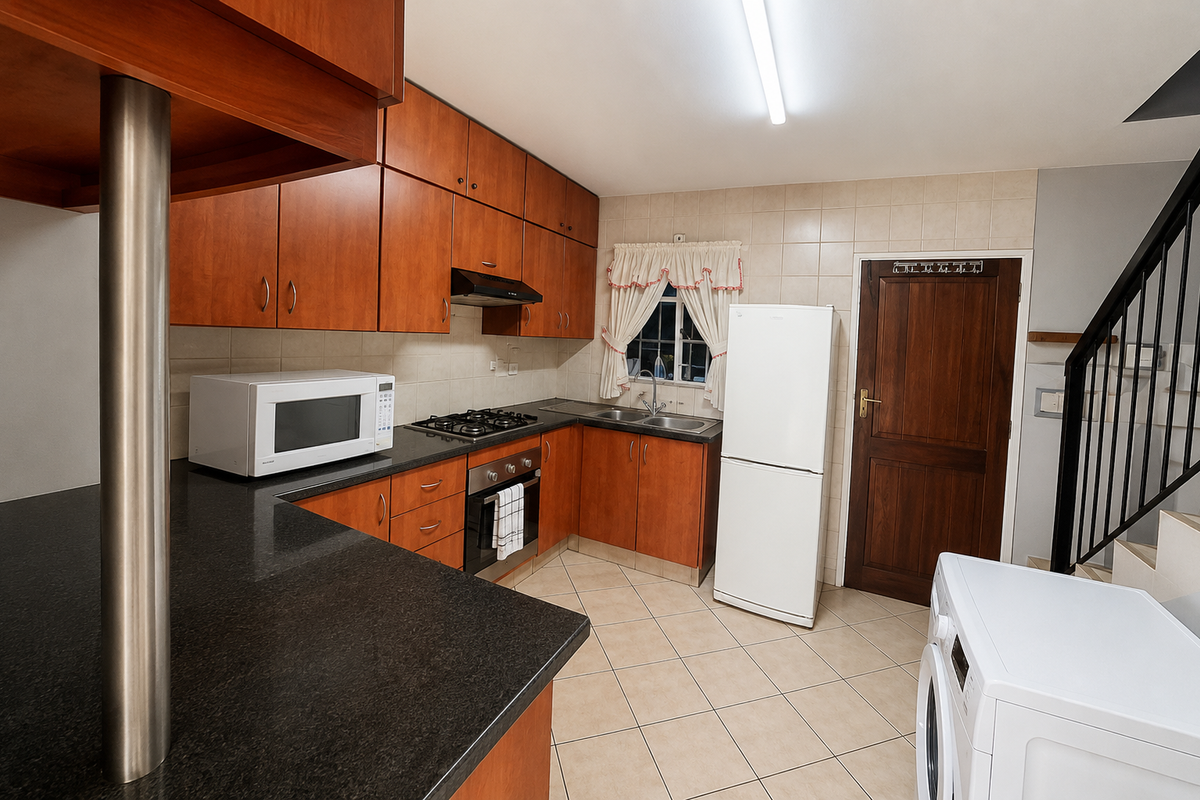 Functional kitchen featuring wood-finish cabinetry, granite countertops, gas hob, built-in oven, and tiled flooring, with an adjacent staircase and direct exterior access.