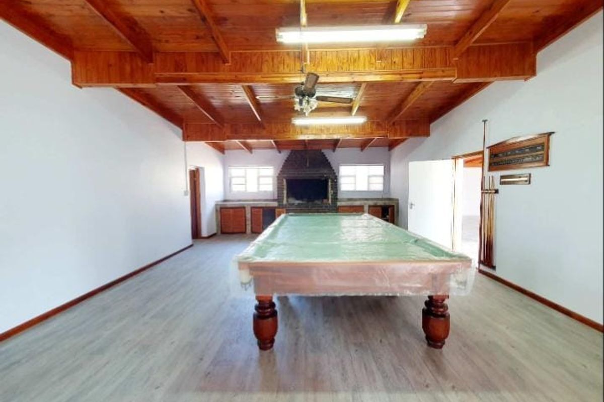 Spacious entertainment room featuring a built-in brick fireplace, exposed timber beam ceiling, and modern light-toned flooring.