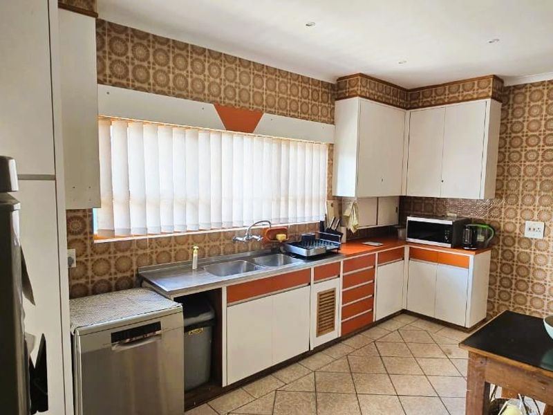 A functional kitchen featuring original cabinetry, double basin sink, and tiled flooring, offering significant potential for a modern renovation.