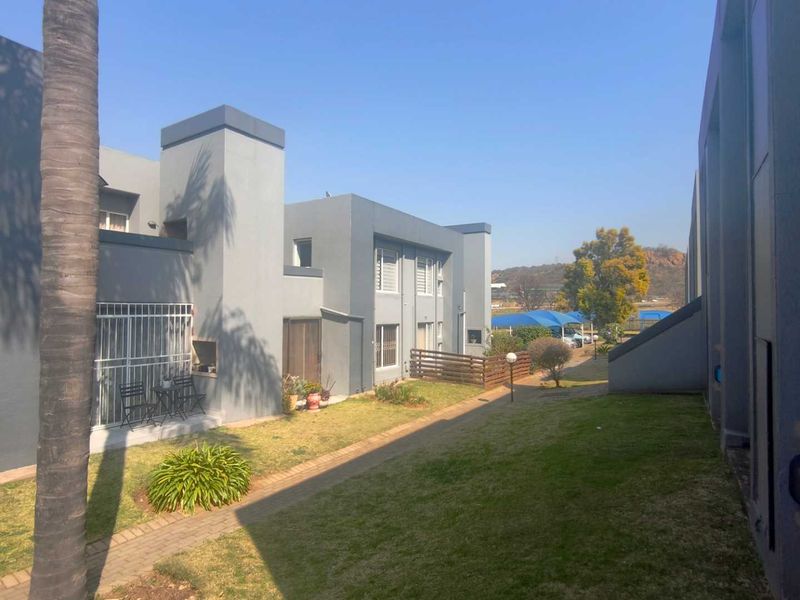 Rear view of the townhouse complex showing a paved walkway, landscaped lawn, and exterior building facades with security features.