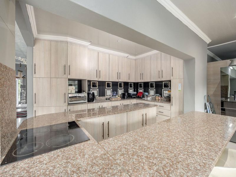 Modern kitchen featuring light wood cabinetry, granite countertops, and a built-in electric hob, offering ample storage and workspace.