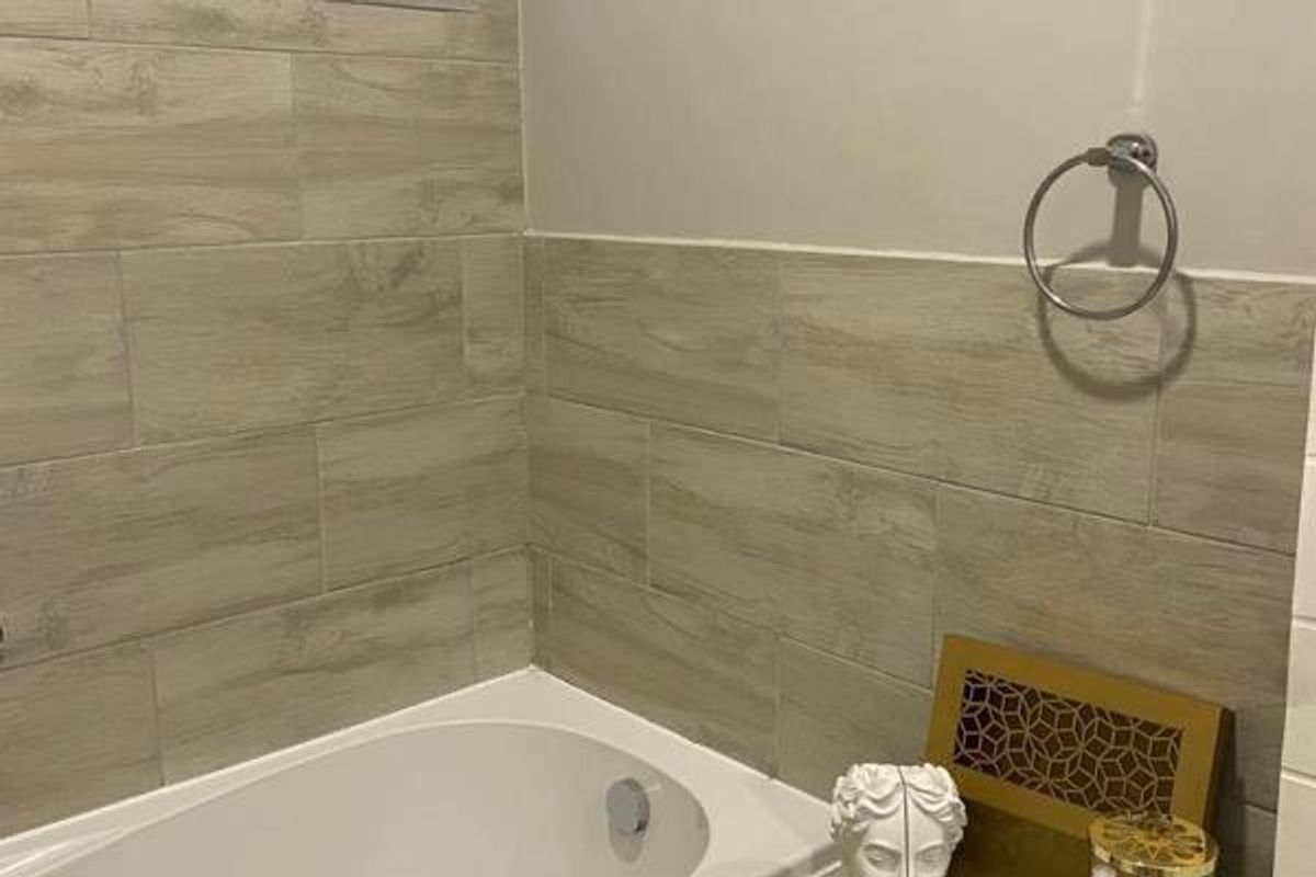A clean bathroom featuring a built-in bathtub with modern wood-look tile wall cladding and a wall-mounted towel ring.
