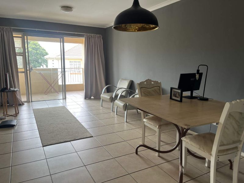 Spacious living area featuring neutral ceramic floor tiles, a large sliding glass door leading to a balcony, and modern grey wall finishes.
