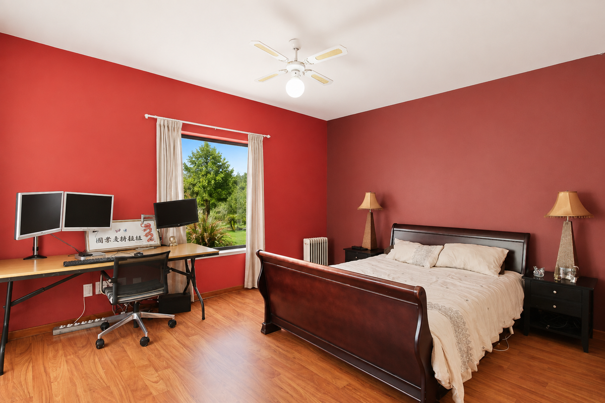 Spacious bedroom featuring laminate flooring, a ceiling fan, and a radiator, with large windows providing natural light and garden views.