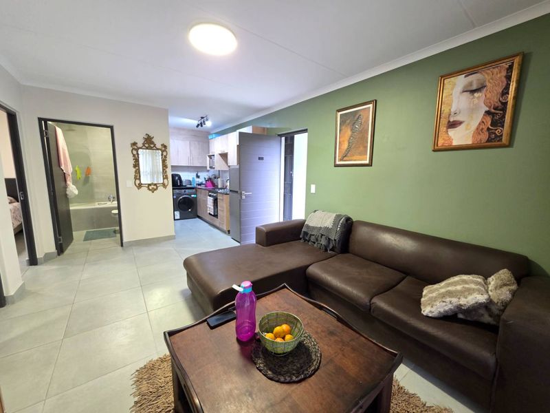 Open-plan living area featuring tiled floors, a modern kitchen with built-in cabinetry, and an integrated laundry space, leading to an adjacent bathroom.