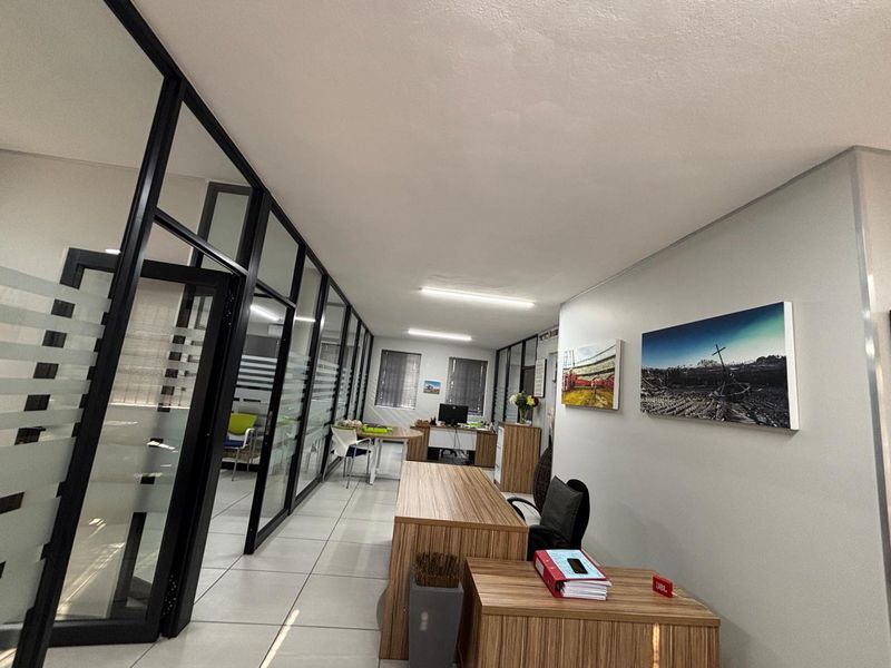 Modern office space featuring black-framed glass partitions, tiled flooring, and bright overhead lighting, creating a professional and open work environment.
