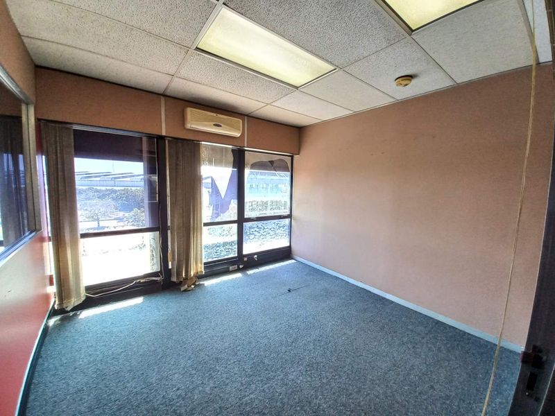 An empty office space featuring a drop ceiling with recessed lighting, wall-mounted air conditioning unit, and large windows with views.