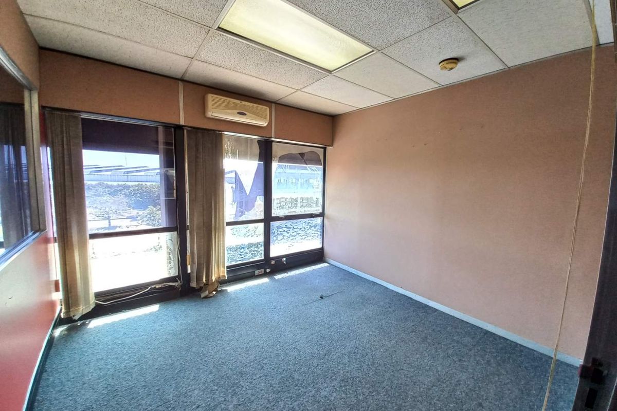 An empty office space featuring a drop ceiling with recessed lighting, wall-mounted air conditioning unit, and large windows with views.