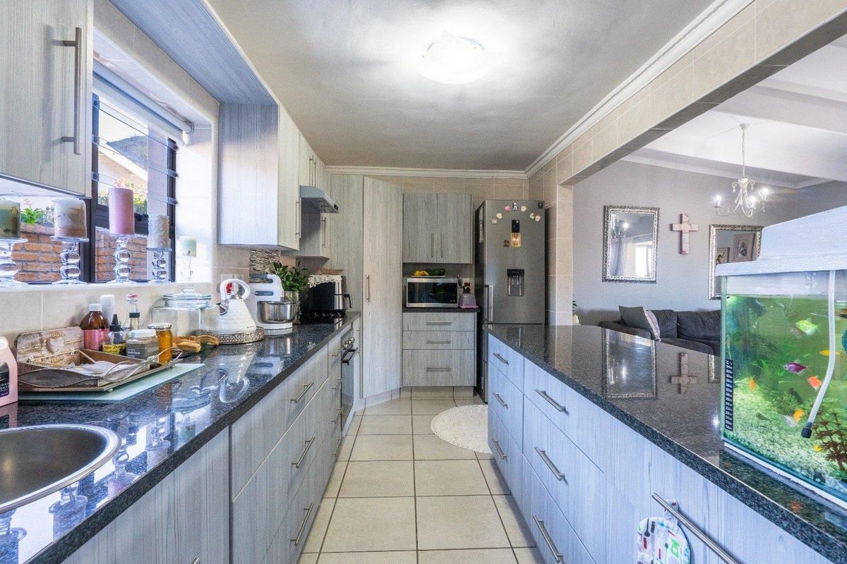 A functional kitchen featuring granite countertops, ample built-in cabinetry, tiled flooring, and an open-plan layout connecting to the adjacent living area.
