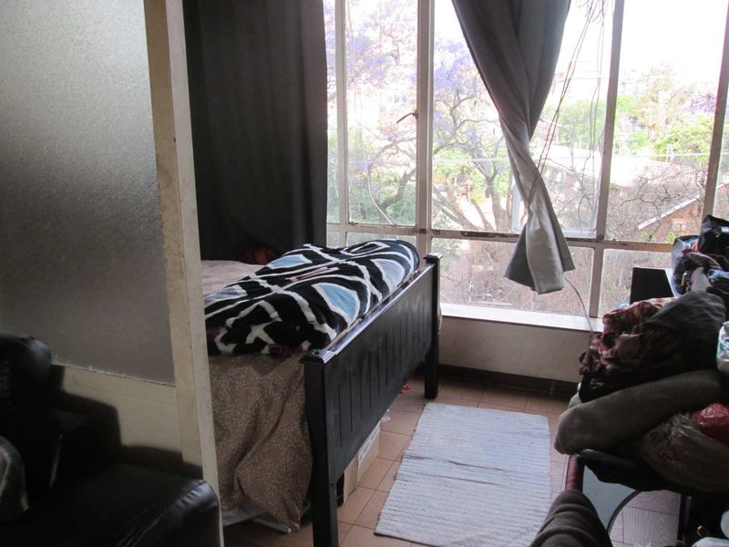 A bedroom featuring large windows with natural light and tiled flooring, offering potential for modernization and improved finishes.