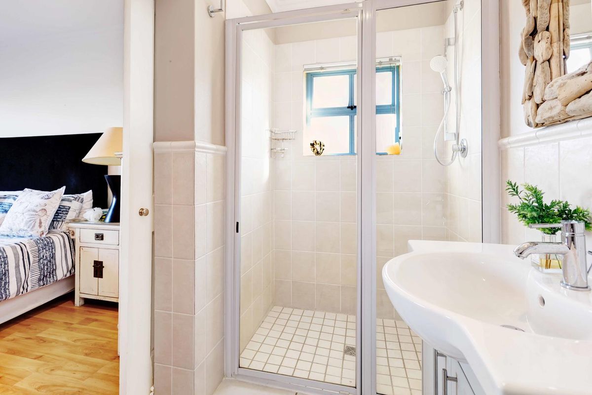 A functional bathroom featuring a tiled shower enclosure and a pedestal basin, with direct access to the adjacent bedroom.