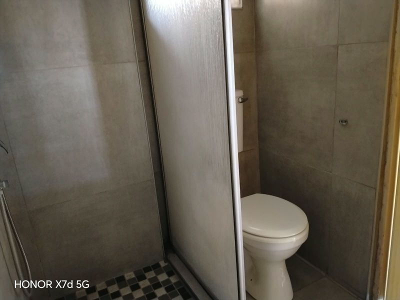 A functional bathroom featuring a shower enclosure and a standard toilet with neutral wall and floor tiling.
