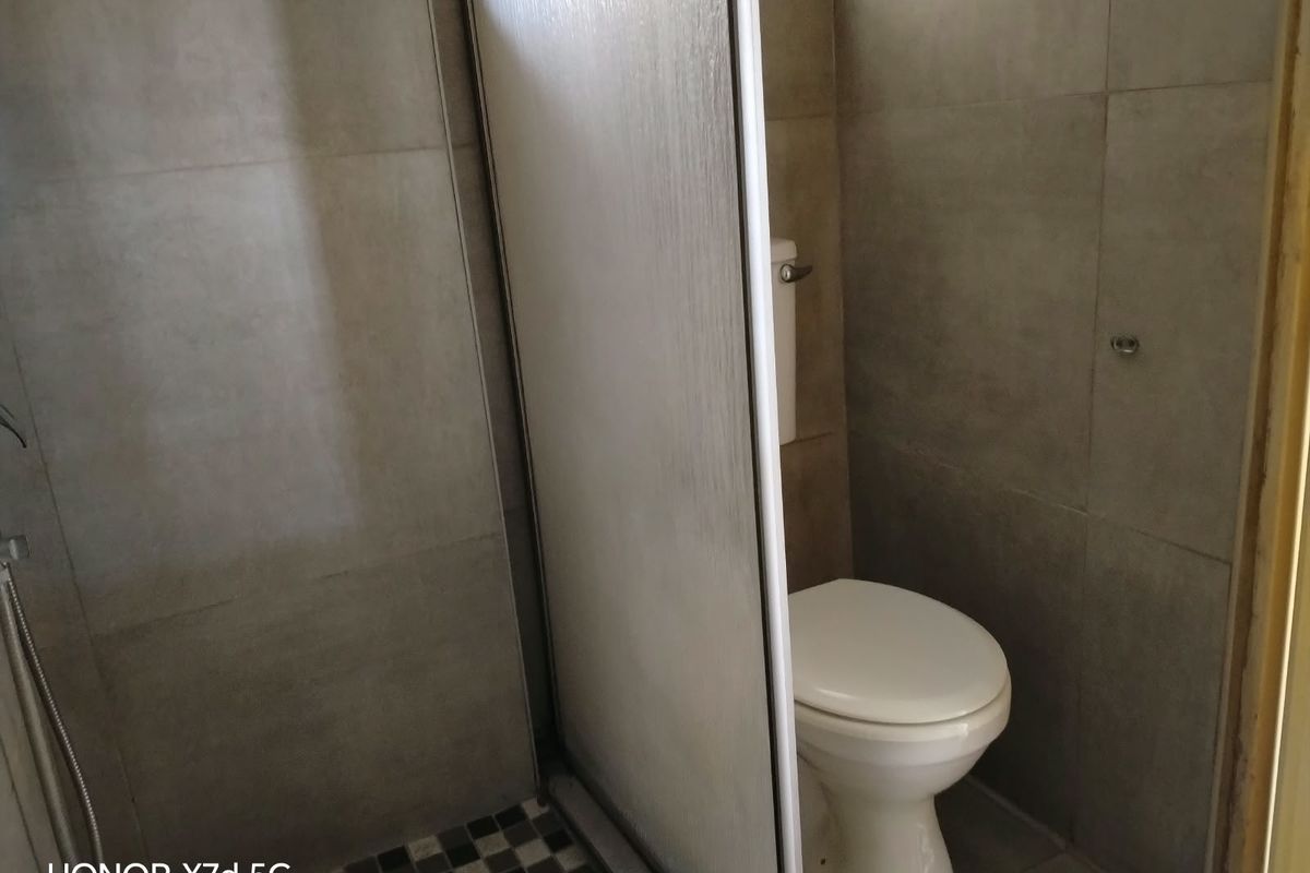 A functional bathroom featuring a shower enclosure and a standard toilet with neutral wall and floor tiling.