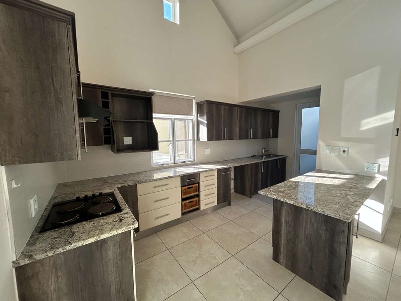 Modern kitchen featuring granite countertops, ample built-in cabinetry, electric hob, and tiled flooring under a high vaulted ceiling.