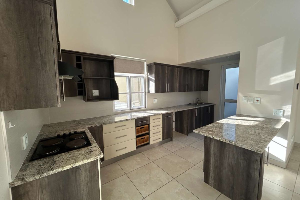 Modern kitchen featuring granite countertops, ample built-in cabinetry, electric hob, and tiled flooring under a high vaulted ceiling.