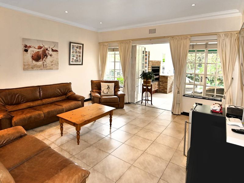 Spacious living room featuring tiled flooring and recessed lighting, with direct access through sliding doors to an outdoor patio area with a built-in braai.