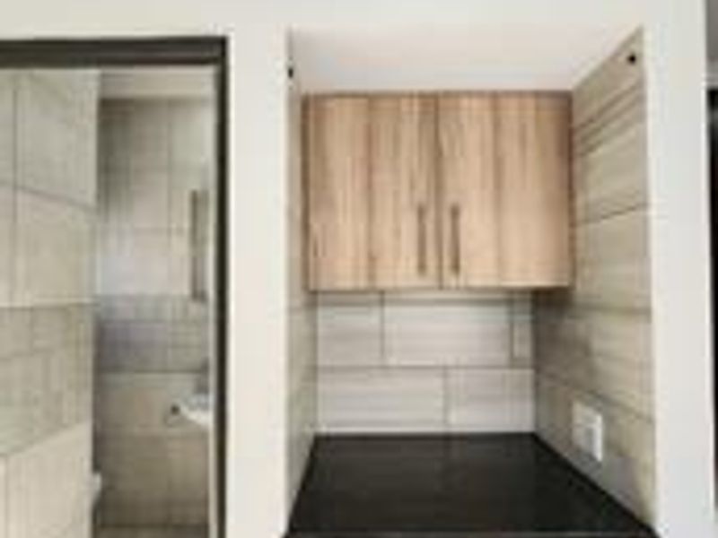 A compact laundry nook featuring built-in wooden cabinetry, a dark stone countertop, and tiled splashback, with plumbing connections for a washing machine.