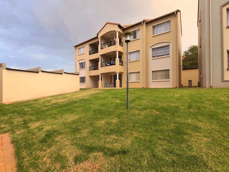 Rear view of a multi-story apartment building featuring private balconies and a well-maintained communal lawn area.