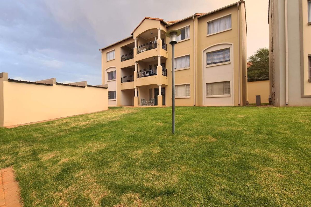 Rear view of a multi-story apartment building featuring private balconies and a well-maintained communal lawn area.