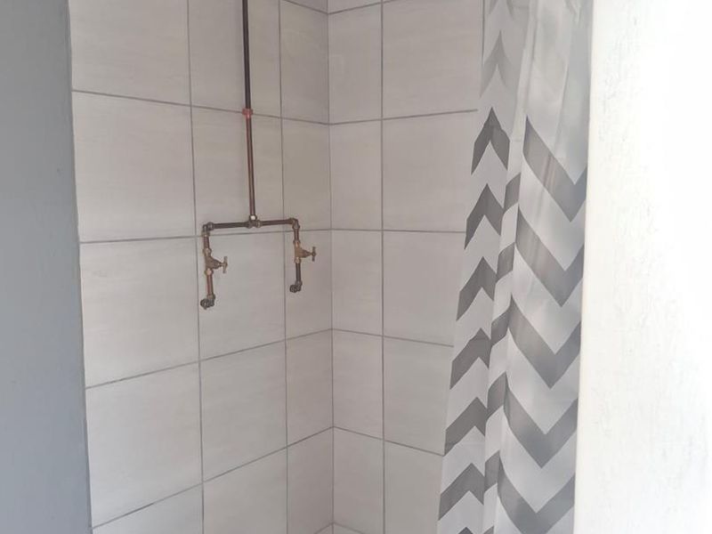 A shower enclosure featuring tiled walls and exposed copper plumbing fixtures.
