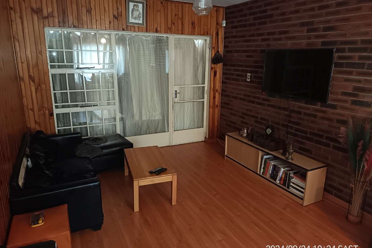 Living room featuring timber wall paneling, an exposed brick feature wall, and laminate flooring with access to an adjacent space via glass doors.