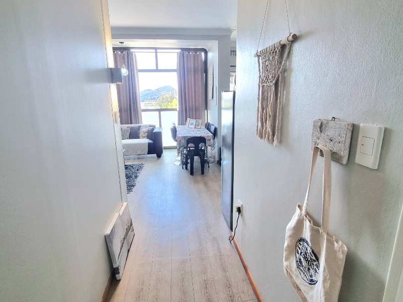 A bright hallway with light-toned laminate flooring leading into an open-plan living and dining area with large windows.