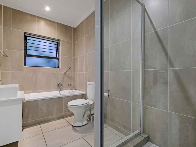 Modern bathroom featuring a built-in bathtub, separate glass shower enclosure, vanity basin, and neutral floor-to-ceiling tiling.
