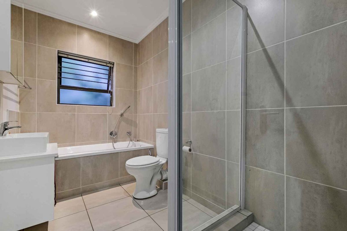 Modern bathroom featuring a built-in bathtub, separate glass shower enclosure, vanity basin, and neutral floor-to-ceiling tiling.
