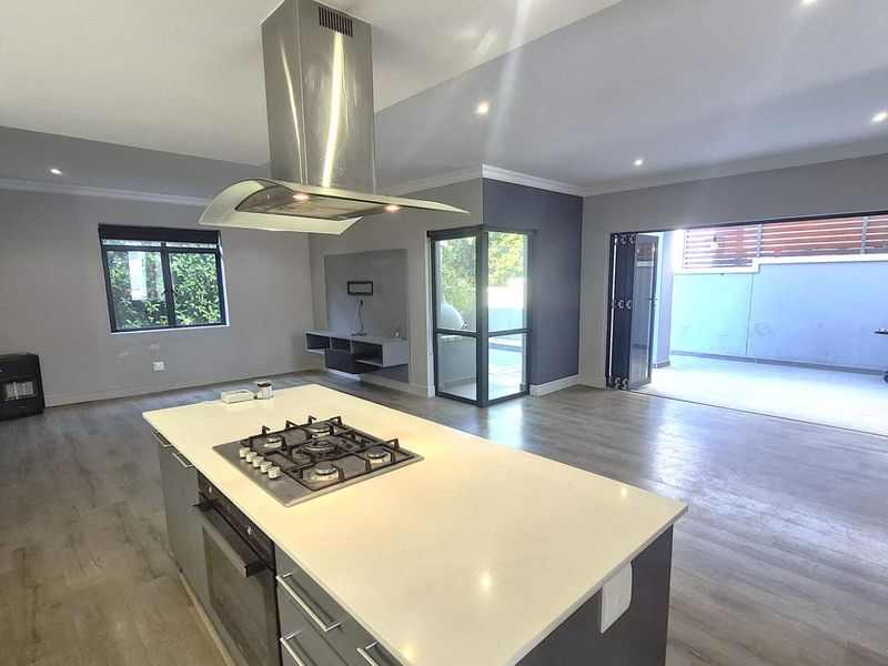 Spacious open-plan living area featuring a modern kitchen island with gas hob, sleek cabinetry, and seamless flow to an outdoor patio through stacking doors.