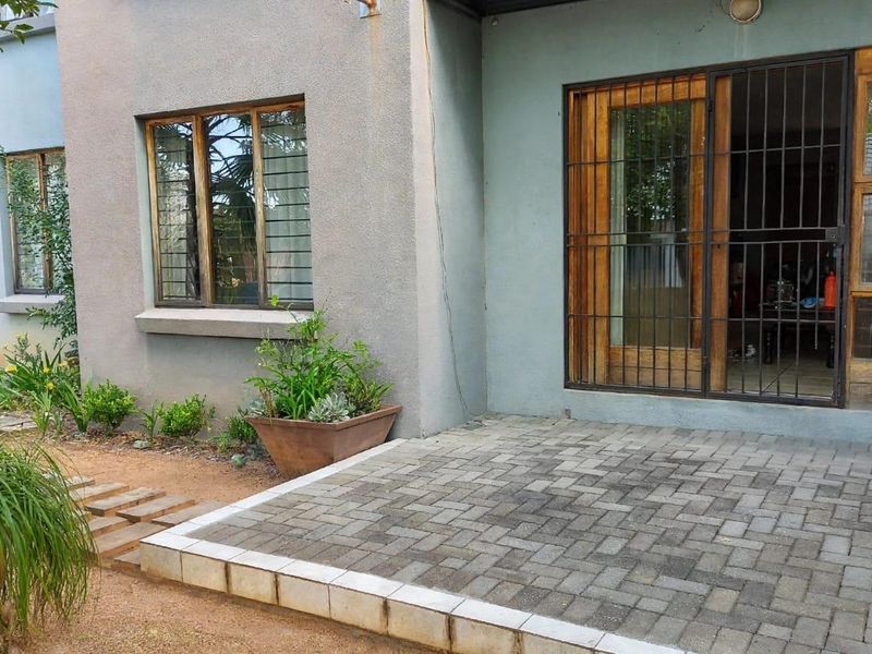 A paved outdoor patio area featuring timber-framed windows and a security gate entrance, providing direct access to the garden.