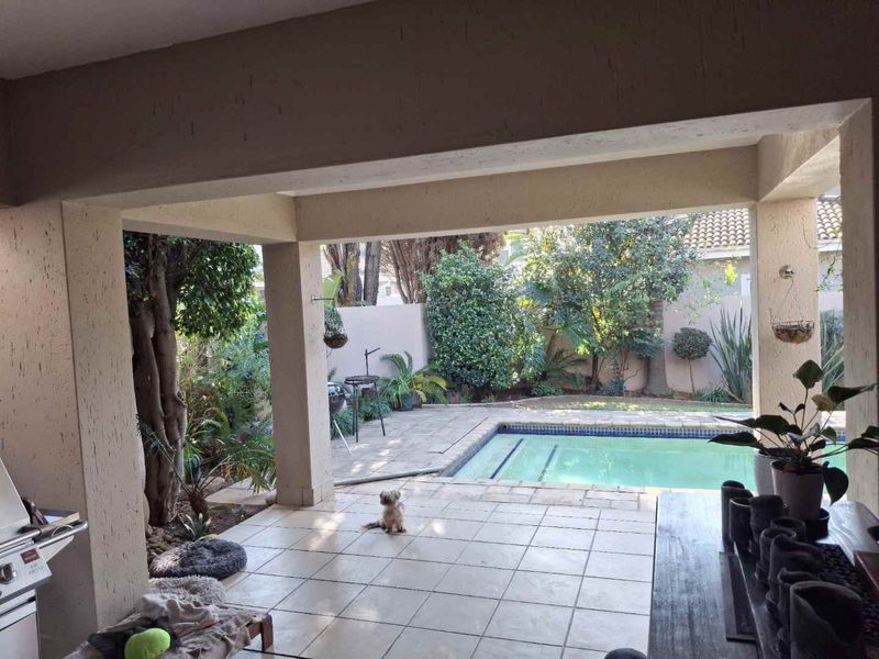 A covered patio area featuring tiled flooring, overlooking a private swimming pool and landscaped garden space.