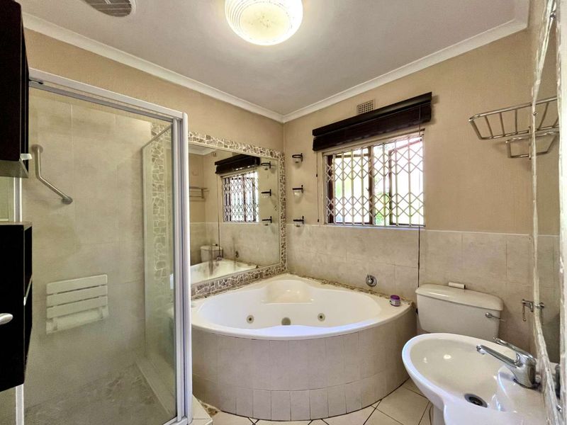 A functional bathroom featuring a corner spa bath, separate glass shower enclosure, pedestal basin, and toilet with tiled finishes.