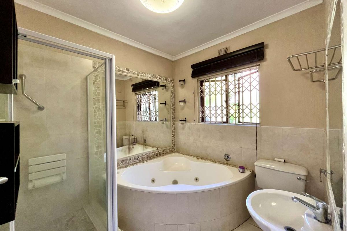 A functional bathroom featuring a corner spa bath, separate glass shower enclosure, pedestal basin, and toilet with tiled finishes.