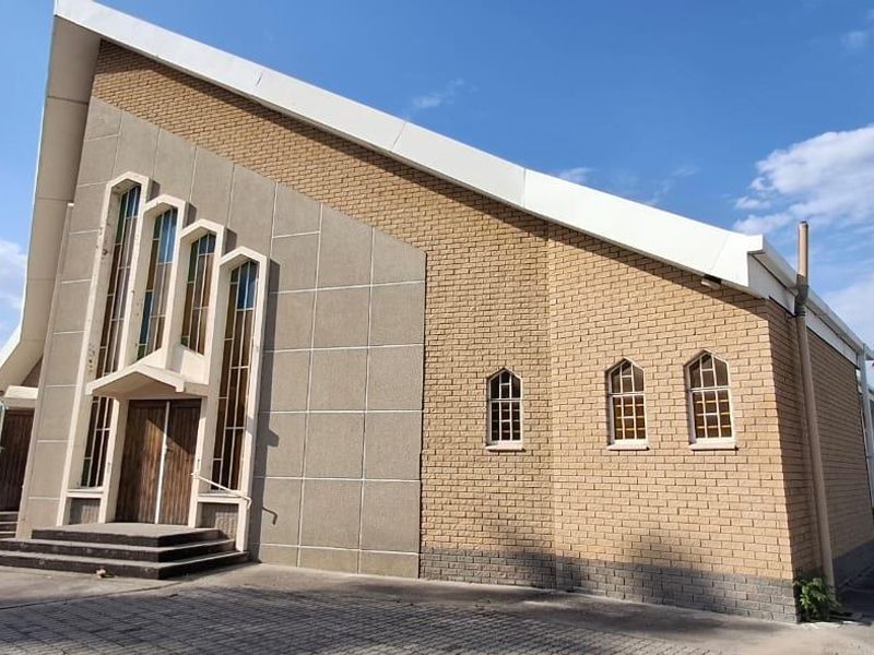 Front exterior view of a mixed-use building featuring a steep pitched roof, brick facade, and arched windows with paved driveway access.