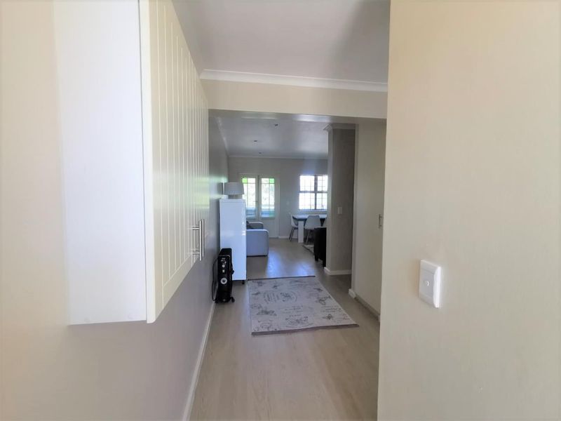 A bright hallway featuring light-toned laminate flooring and built-in cabinetry, providing a clean transition into the open-plan living and dining area.